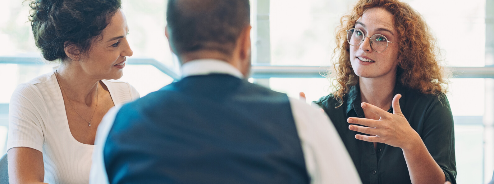 A group of people in discussion. A woman is leading the conversation and gesturing to the group, smiling