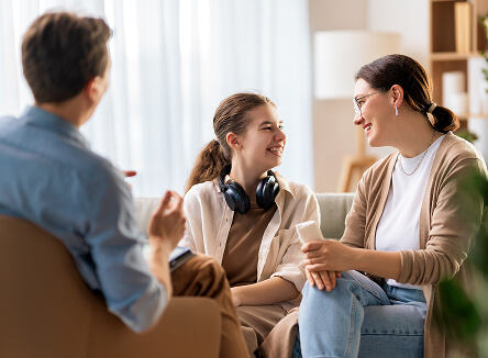A mother and daughter smiling at each other. A professional facing away from camera is observing.