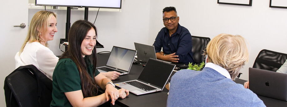Shanker Pragnaratne and three Prag Consulting coworkers smiling in a meeting around a large workspace